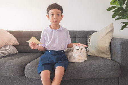 Happy Asian boy 6-7 years old, black-haired, fair-skinned, wearing a white shirt, blue shorts and his British Shorthair cat looking at the camera. concept about education, playing, creativity, pets.の写真素材