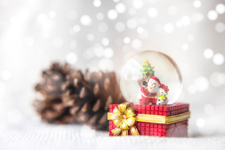 Christmas balls, Santa Claus in a Snow globe, and Pine cones on a white Cloth, set Against a Red Background and exquisite bokeh. New Year Celebration Atmosphere, about of Important day.の写真素材