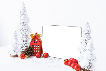 Tapelet with a white screen mock-up and White calendar with a festive scene of a beautiful Christmas tree adorned, with Christmas balls, pine cones, and a red house gift box.の写真素材