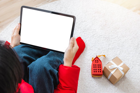 A woman shopping online sitting on carpet at home with a tablet with a white screen isolated. Use your credit card to tap the screen to verify your identity. Clipping Path.の写真素材