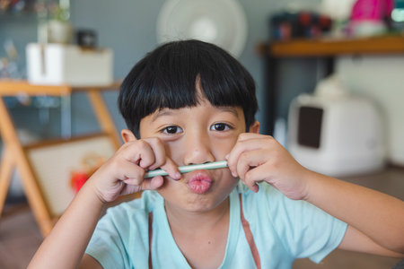 Close up portrait of Asian boy with black bangs, black eyes with a smiling face wearing a light green shirt look at camera and sitting on the floor of his house and hand holding pencil to draw.の写真素材