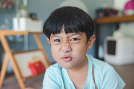 Close up portrait of Asian boy with black bangs, black eyes with a smiling face wearing a light green shirt look at camera and sitting on the floor of his house and hand holding pencil to draw.の写真素材