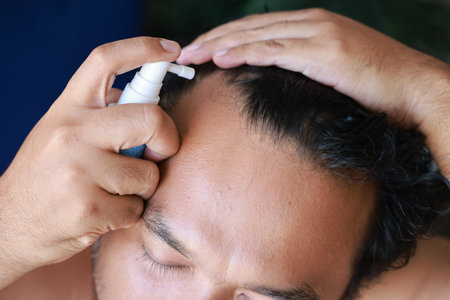 Asian men use serum spray to maintain strong hair and prevent breakage. Man with worry and touching...