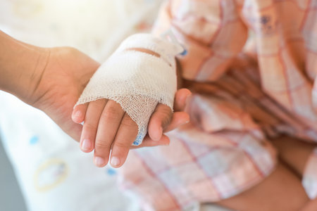 Mother holds the hand of her sick child with concern in Hospital ward. tube of normal saline infusion at the hospital because it is influenza A. Concept about treatment, emergency, medical, chemotherapy, sick.の写真素材