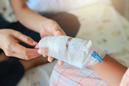Mother holds the hand of her sick child with concern in Hospital ward. tube of normal saline infusion at the hospital because it is influenza A. Concept about treatment, emergency, medical, chemotherapy, sick.の写真素材