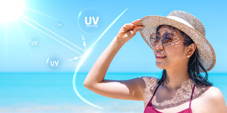 Asian woman in sun hat and sunglasses smiling on beach under bright sunlight with UV protection...