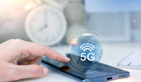 Hand touching smartphone with 5G icon and global network interface, representing high-speed wireless...