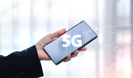 Hand holding smartphone with 5G icon and global network interface, representing high-speed wireless...