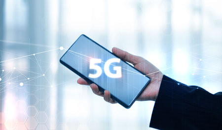 Hand holding smartphone with 5G icon and global network interface, representing high-speed wireless...