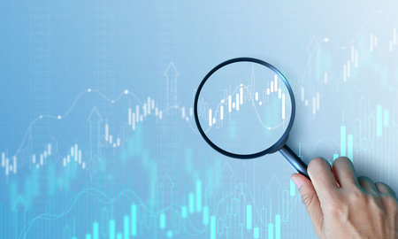 Hand holding magnifying glass analyzing digital financial stock chart. Data analysis, investment...