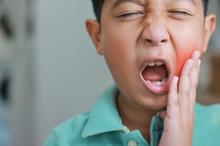 Asian boy suffering from severe toothache with red highlight on cheek, child having dental problem, tooth decay, gum inflammation, sensitive teeth or wisdom tooth pain and crying at home.の写真素材