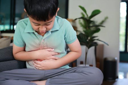 Asian boy holding belly suffering from severe abdominal pain with red inflamed area. Concept of stomach ache, indigestion, food poisoning, gastritis, and pediatric medical healthcare treatment.の写真素材