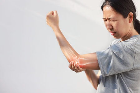 Asian woman suffering from elbow joint pain with red x-ray bone graphic overlay, female touching arm feeling ache from inflammation, arthritis, tendonitis or injury in garden, healthcare concept.の写真素材