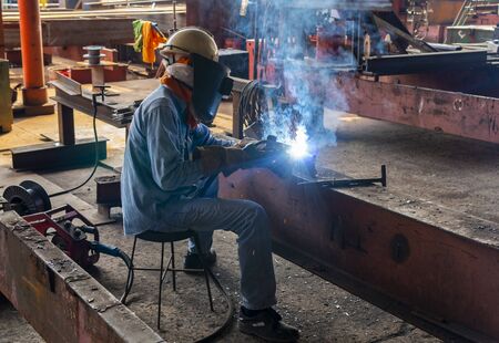 The welder is welding a steel structure work with process Flux Cored Arc Welding(FCAW) and dressed properly with personal protective equipment(PPE) for safety, at industrial factory.の写真素材