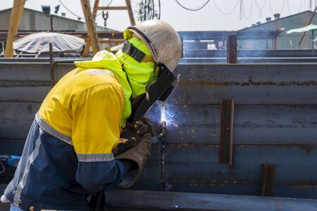 The welder is welding a steel structure work with process Flux Cored Arc Welding(FCAW) and dressed properly with personal protective equipment(PPE) for safety, at industrial factory.の写真素材