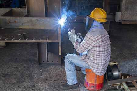 The welder is welding a steel structure work with process Flux Cored Arc Welding(FCAW) and dressed properly with personal protective equipment(PPE) for safety, at industrial factory.の写真素材