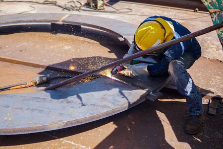 Welder is gouging back weld with Air carbon arc gouging machine and dressed properly with personal protective equipment(PPE) for safety, at industrial factory.の写真素材