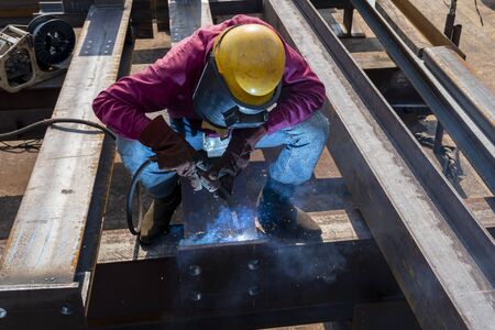 The welder is welding a steel structure work with process Flux Cored Arc Welding(FCAW) and dressed properly with personal protective equipment(PPE) for safety, at industrial factory.の写真素材