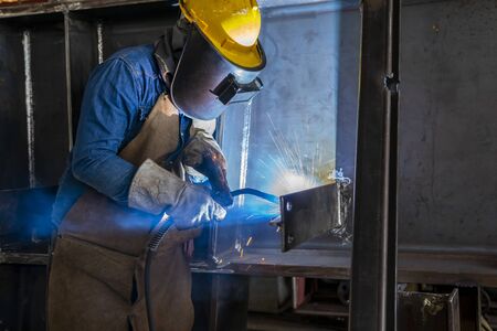 The welder is welding a steel structure work with process Flux Cored Arc Welding(FCAW) and dressed properly with personal protective equipment(PPE) for safety, at industrial factory.の写真素材