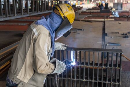 The welder is welding a steel structure work with process Flux Cored Arc Welding(FCAW) and dressed properly with personal protective equipment(PPE) for safety, at industrial factory.の写真素材