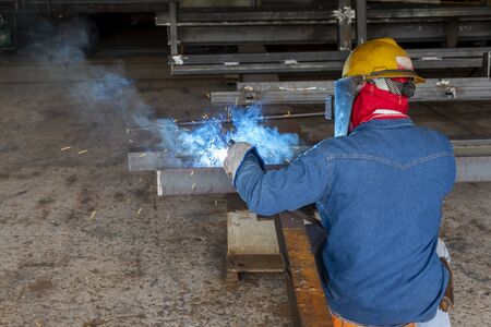 The welder is welding a steel structure work with process Flux Cored Arc Welding(FCAW) and dressed properly with personal protective equipment(PPE) for safety, at industrial factory.の写真素材