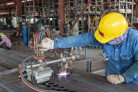 Workers are using gas cutting machines to burning bending steel plates that is curled after welding for built-up h-beam at industrial factory.の写真素材