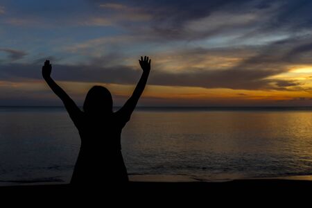 Silhouette of a woman are standing raise two hands at the seaside and the sunset is background.