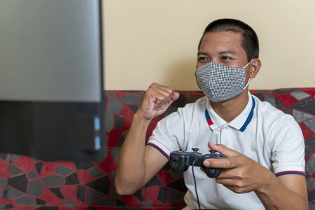 Men wears medical protective mask and playing games during quarantine time at home. to reduce the...