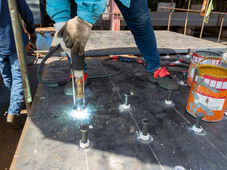 A welder is using a Stud Welding Machine to weld stud bolt on steel plate, at industrial factory.