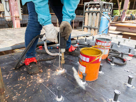 A welder is using a Stud Welding Machine to weld stud bolt on steel plate, at industrial factory.