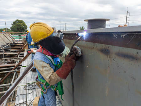 The welder is welding a steel structure work with process Flux Cored Arc Welding(FCAW) and dressed properly with personal protective equipment(PPE) for safety, at industrial factory.の写真素材