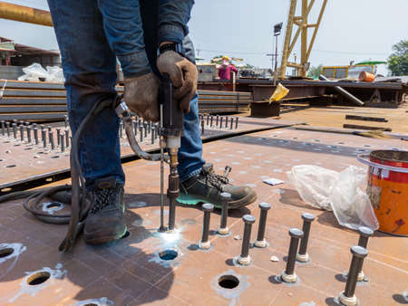 A welder is using a Stud Welding Machine to weld stud bolt on steel plate, at industrial factory.の写真素材