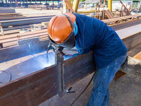 The welder is welding add joint of steel H-beam with process Flux Cored Arc Welding(FCAW) and...