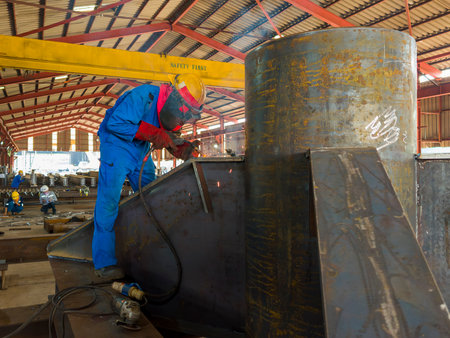 Welder is welding a steel plate for steel structure work with process Flux Cored Arc Welding(FCAW) and dressed properly with personal protective equipment(PPE) for safety, at industrial factory.の写真素材