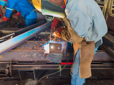 Welder welding a steel plate for steel structure work with process Flux Cored Arc Welding(FCAW) and appropriately dressed with personal protective equipment(PPE) for safety, at an industrial factory.の写真素材
