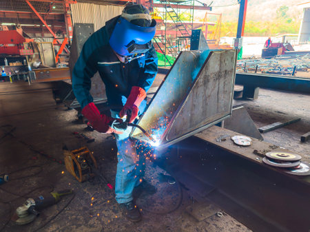 Welder Welding Steel Plate for Steel Structure Work with Process Flux Cored Arc Welding (FCAW) and Appropriately Dressed with Personal Protective Equipment (PPE) for Safety, at an Industrial Factory.の写真素材
