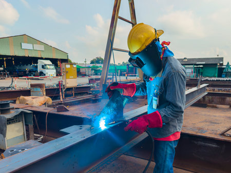 Welder Welding Steel Plate for Steel Structure Work with Process Flux Cored Arc Welding (FCAW) and Appropriately Dressed with Personal Protective Equipment (PPE) for Safety, at an Industrial Factory.の写真素材