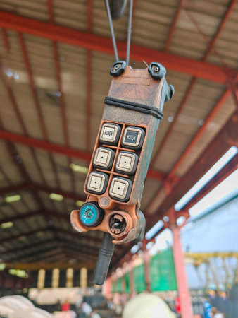 Close-up of a damaged remote control for an overhead crane, showing worn and broken buttons inside an industrial factory setting.の写真素材