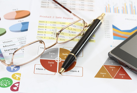 closeup image of graphics and finance report for business with pen mobile phone and coffeeの写真素材