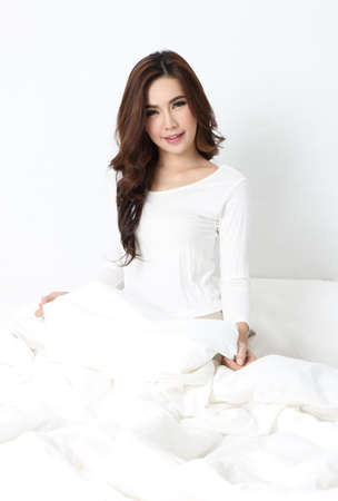 young beautiful asian woman sitting on the bed and white roomの写真素材