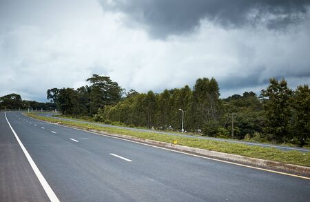 Empty asphalt road in countryside, bend of road, field in the background, gray cloudの写真素材