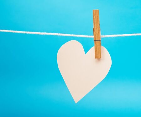 Paper pink heart hanging on twine against blue paper texture for Valentines day