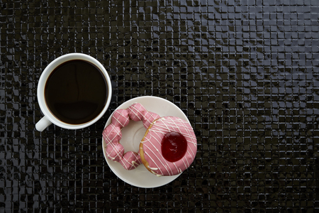 Cup of black coffee with pink donuts  are on black ceramic tilesの写真素材