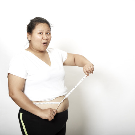 Woman measuring her waistline fat tummy on white background,obese womenの写真素材
