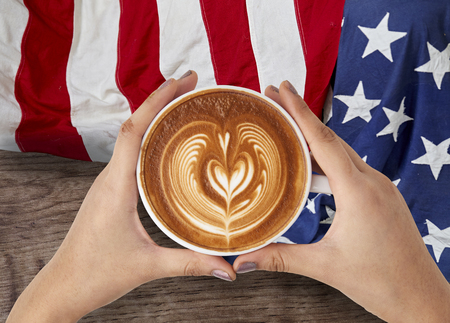 Latte art in a woman's hands With the flag of america on wooden backgroundの写真素材