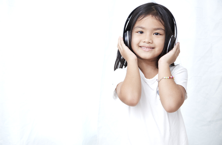 Cute little girl with smartphone and headphones listening to music and dancingの写真素材