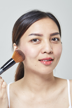 Asian woman face portrait beauty skin care and applying cosmetic powder brush on white background. Natural makeup, skincare, cosmetology and plastic surgery concept.の写真素材