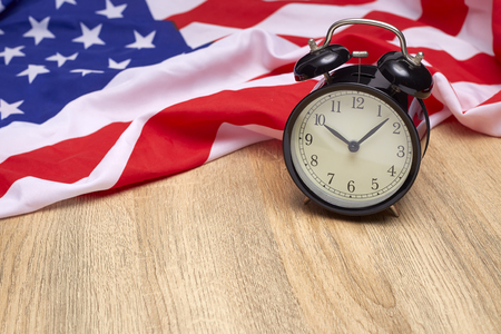 National flag of America and black alarm clock on old wooden backgroundの写真素材