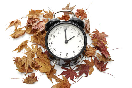 Image of autumn Time Change, Fall back concept, Dry leaves and vintage alarm Black Clock on wooden...