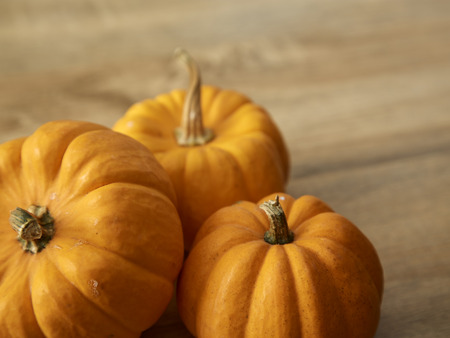 Bright yellow and orange color three ripe pumpkins with stem on light brown wooden table, with free space for design and textの写真素材
